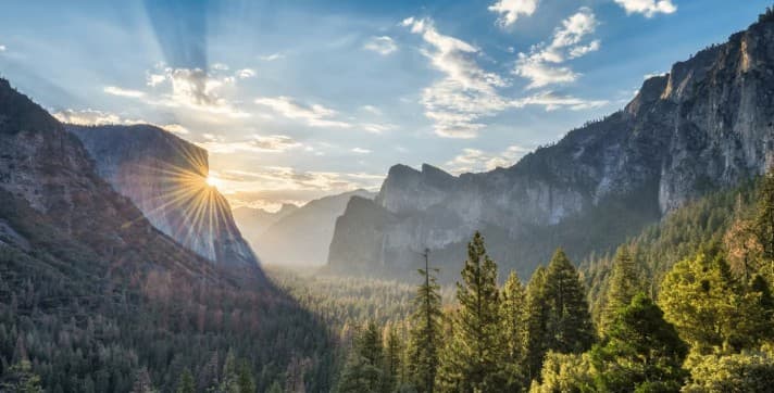 Morning sunlight breaking across Yosemite Valley and pine-covered cliffs